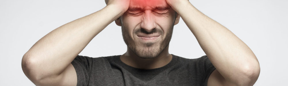 Young man isolated on gray background, showing how much head hurts, experiencing pain, looking miserable and exhausted. Headache concept.